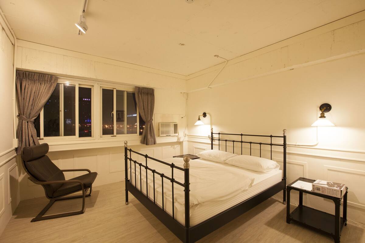 A bedroom with a single bed, a chair, a nightstand, and a window with curtains.