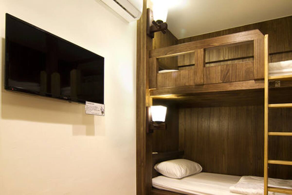 A bunk bed with a wooden headboard, a small shelf above the bed, and a wall-mounted television.