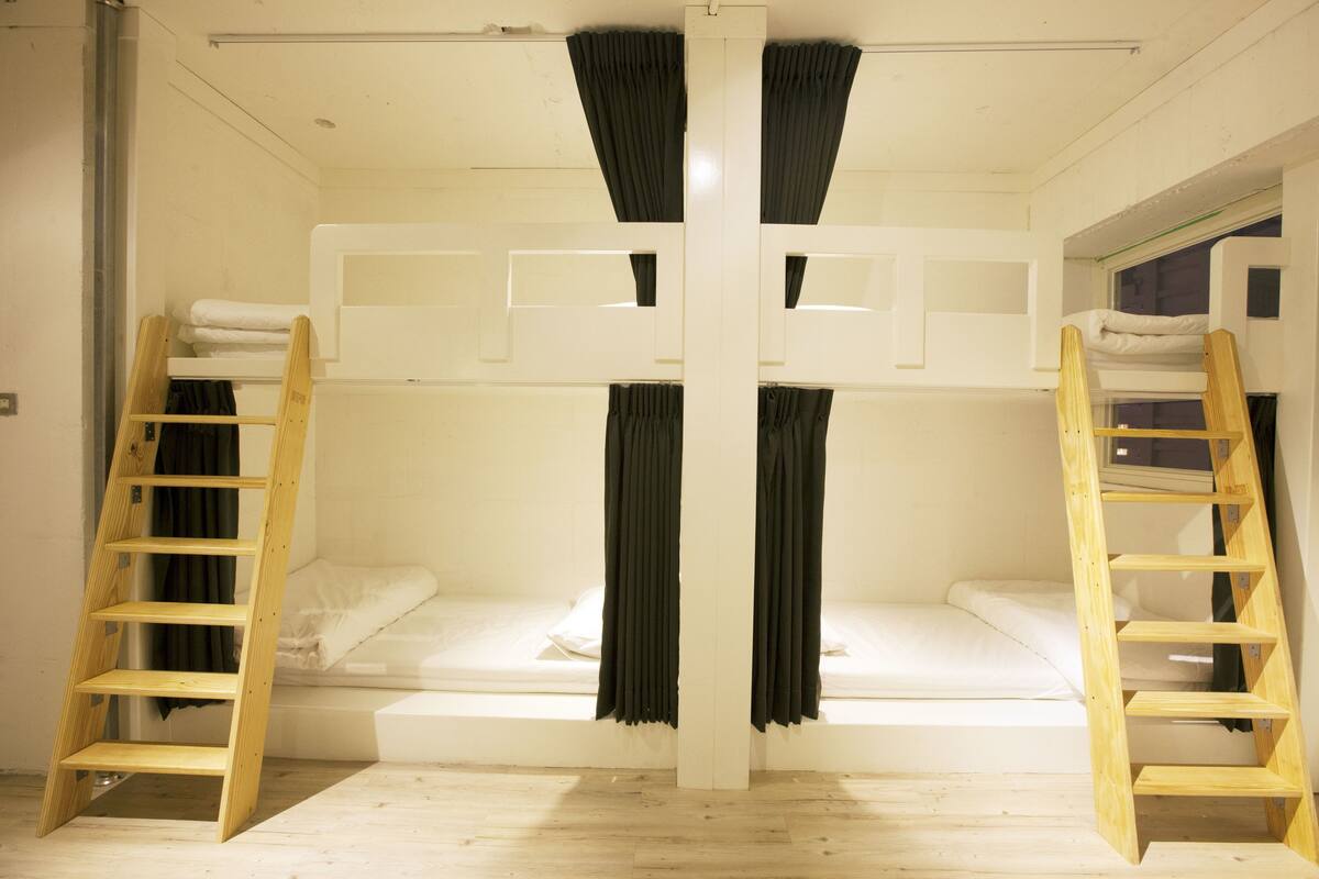 A bunk bed room with two wooden ladders, white bedding, and black curtains.
