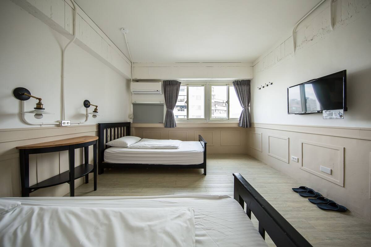 A bedroom with a bed, a desk, a TV, and a window with curtains.