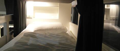 A single bed with a headboard, a bedside table, and a window with curtains.