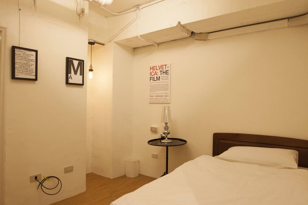 A bedroom with a wooden bed, white bedding, a framed picture on the wall, and a poster.