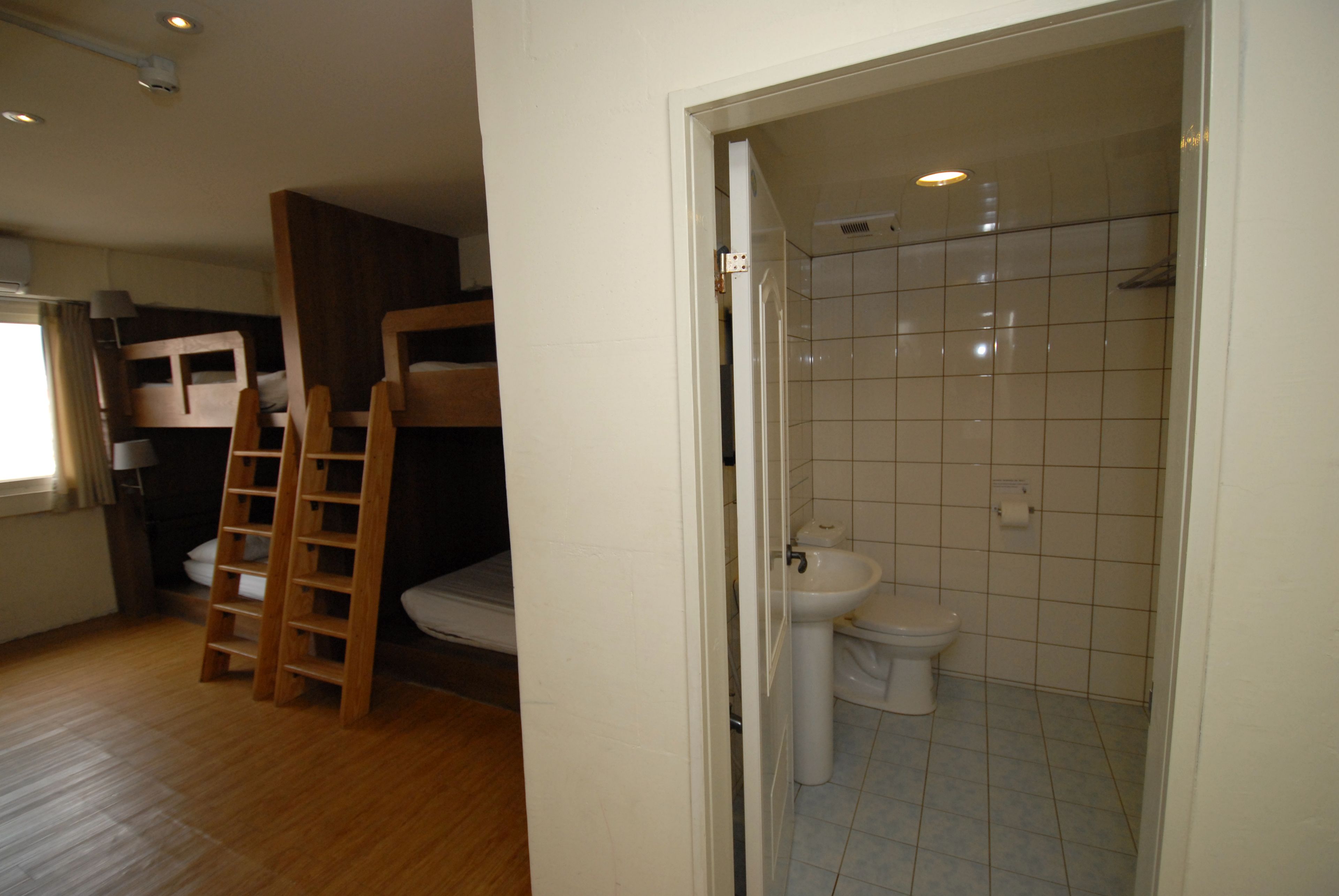 Une pièce avec un lit superposé en bois, une échelle, un lavabo et des toilettes.