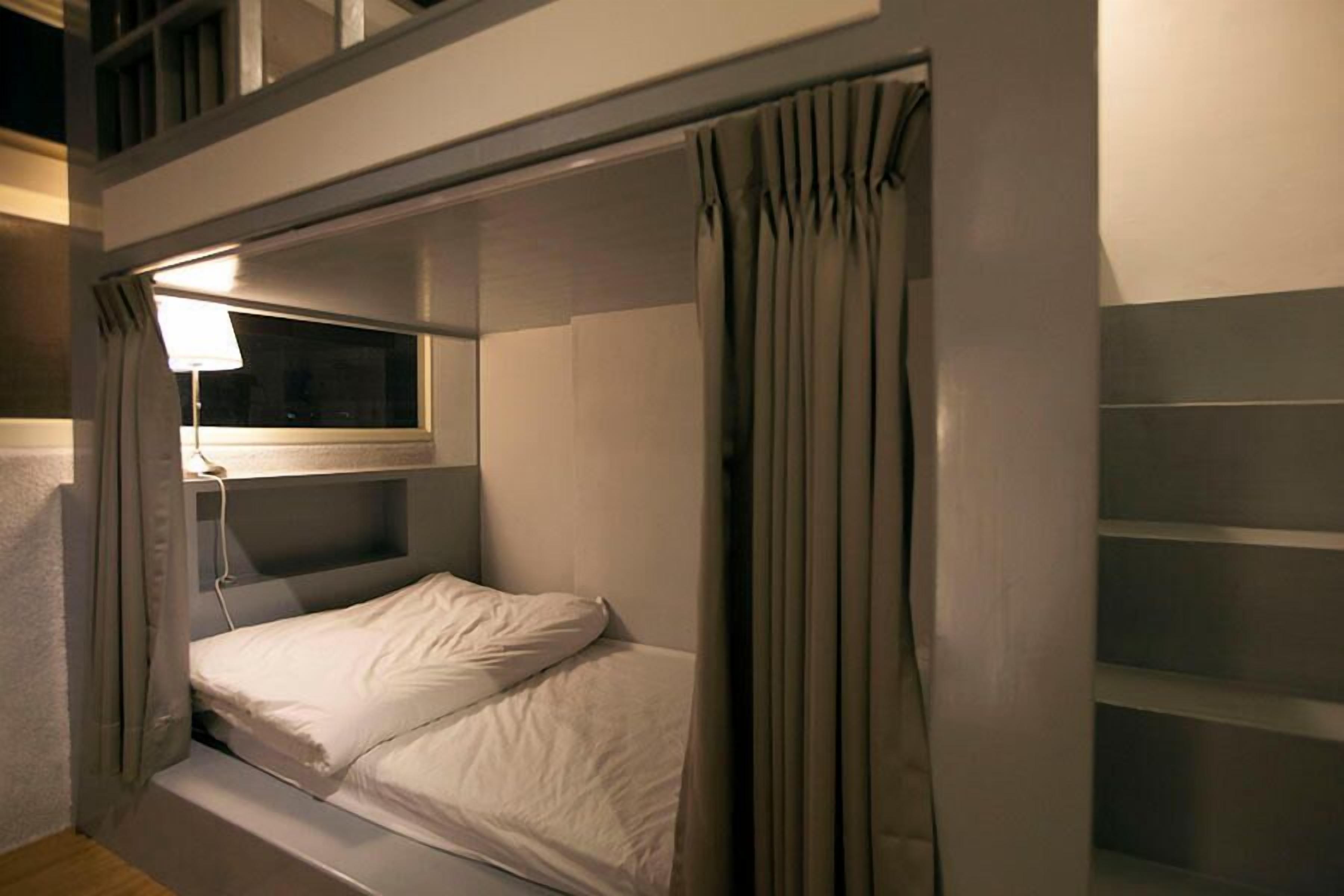 A bunk bed with a window and a lamp, curtains, and a shelf.