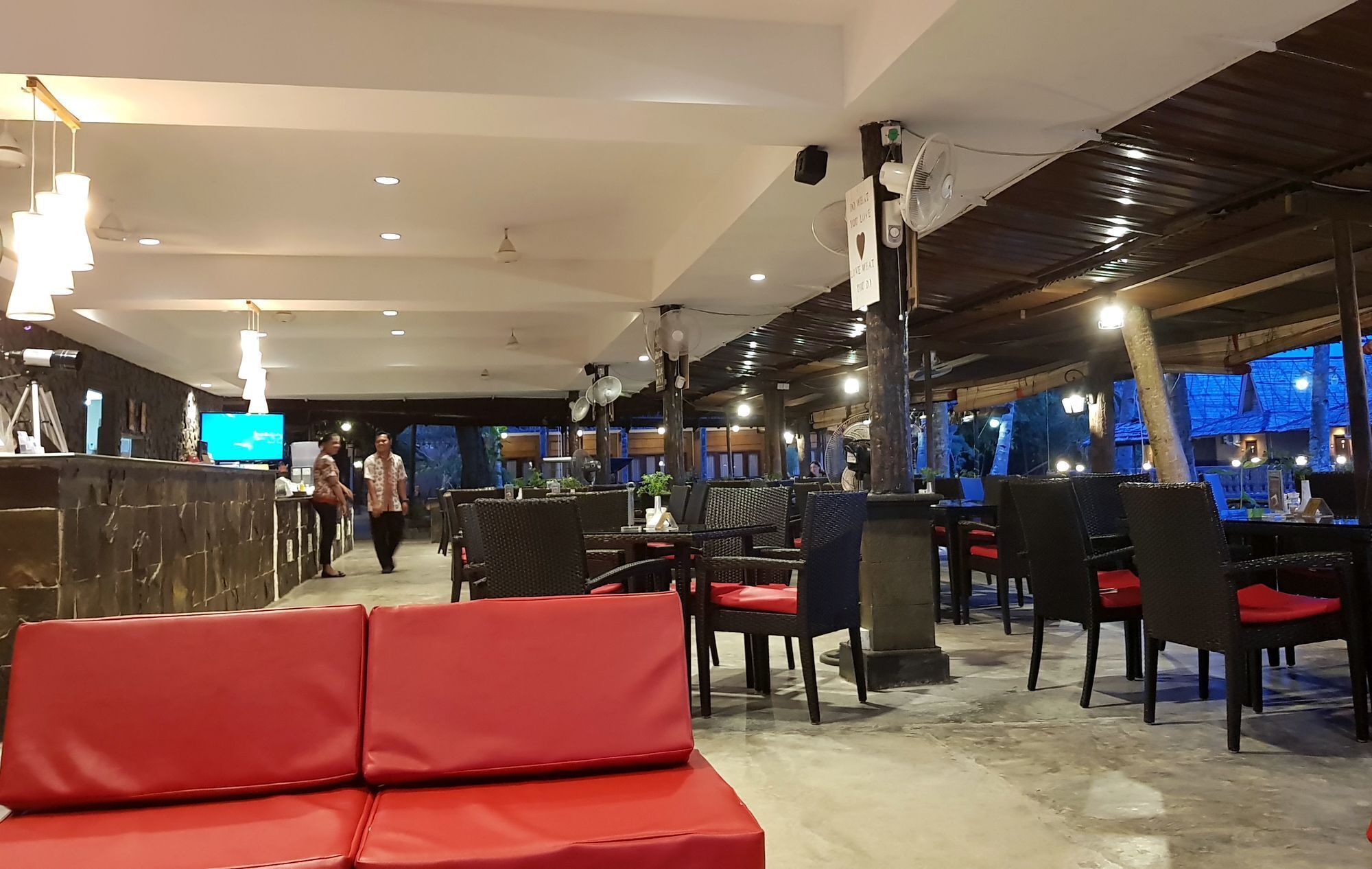 Un restaurante con zona de bar, asientos rojos y ventiladores de techo.
