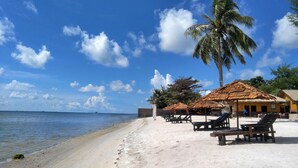 A beach with thatched-roof huts, palm trees, and lounge chairs. - Bintan SpaVilla Beach Resort (Bintan)