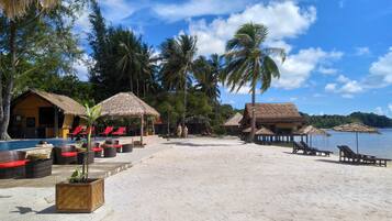 A beach resort with thatched-roof huts, lounge chairs, and a swimming pool.