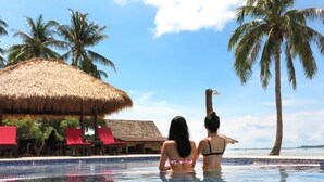 A swimming pool with two people, palm trees, and a thatched-roof structure. - Bintan SpaVilla Beach Resort (Bintan)