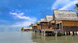 Overwater bungalows with wooden roofs and thatched walls, connected by a wooden walkway over calm water. - Bintan SpaVilla Beach Resort (Bintan)