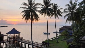 A resort with a wooden pier, palm trees, and a view of the sunset over the water. - Bintan SpaVilla Beach Resort (Bintan)