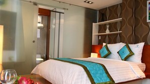 Habitación de hotel moderna con cama, mesita de noche con una copa de vino y fruta, y un panel decorativo en la pared.