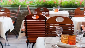 Un área de comedor al aire libre con sillas y mesas de madera, rodeada por un jardín con flores rosadas.