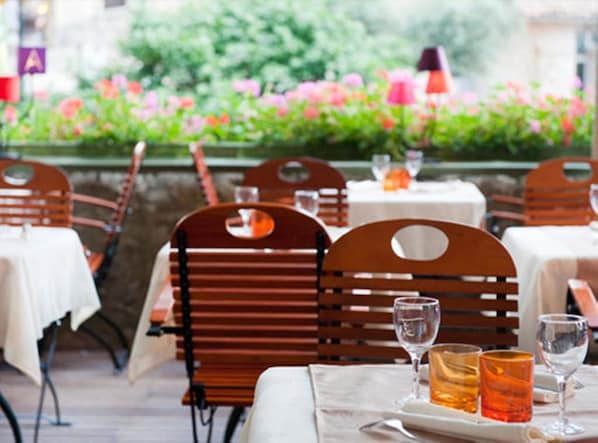 An outdoor dining area with wooden chairs and tables, surrounded by a garden with pink flowers.