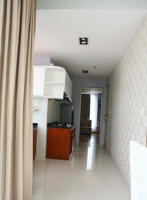A narrow hallway with a kitchenette on the left, a door at the end, and patterned wallpaper on the right.