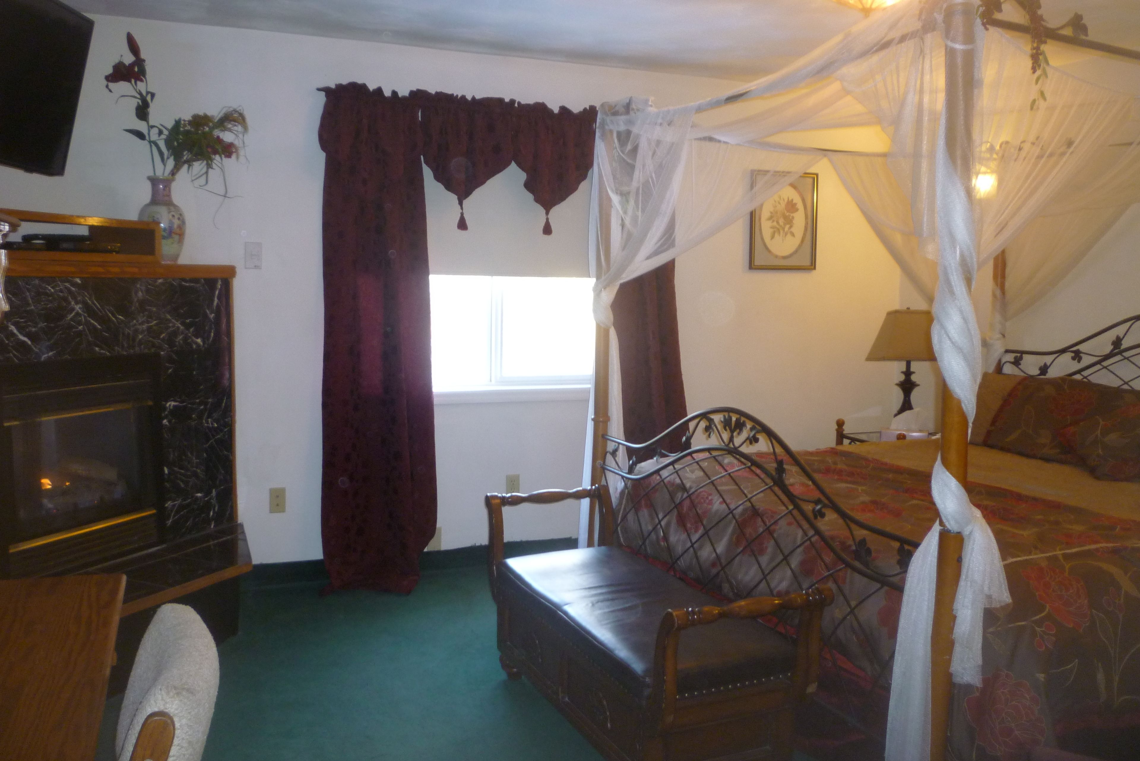 A bedroom with a canopy bed, a wooden bench, a television, and a vase with flowers.