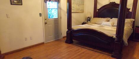 A four-poster bed with a dark wooden frame, a window with a plaid curtain, and a painting on the wall.