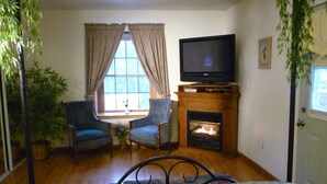 A room with a bed, two chairs, a television, a fireplace, and a window with curtains. - Fairbanks Extended Stay (Fairbanks)
