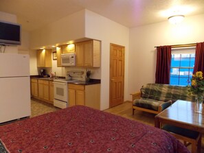 A compact room with a kitchenette, a bed, a sofa, and a window with curtains.