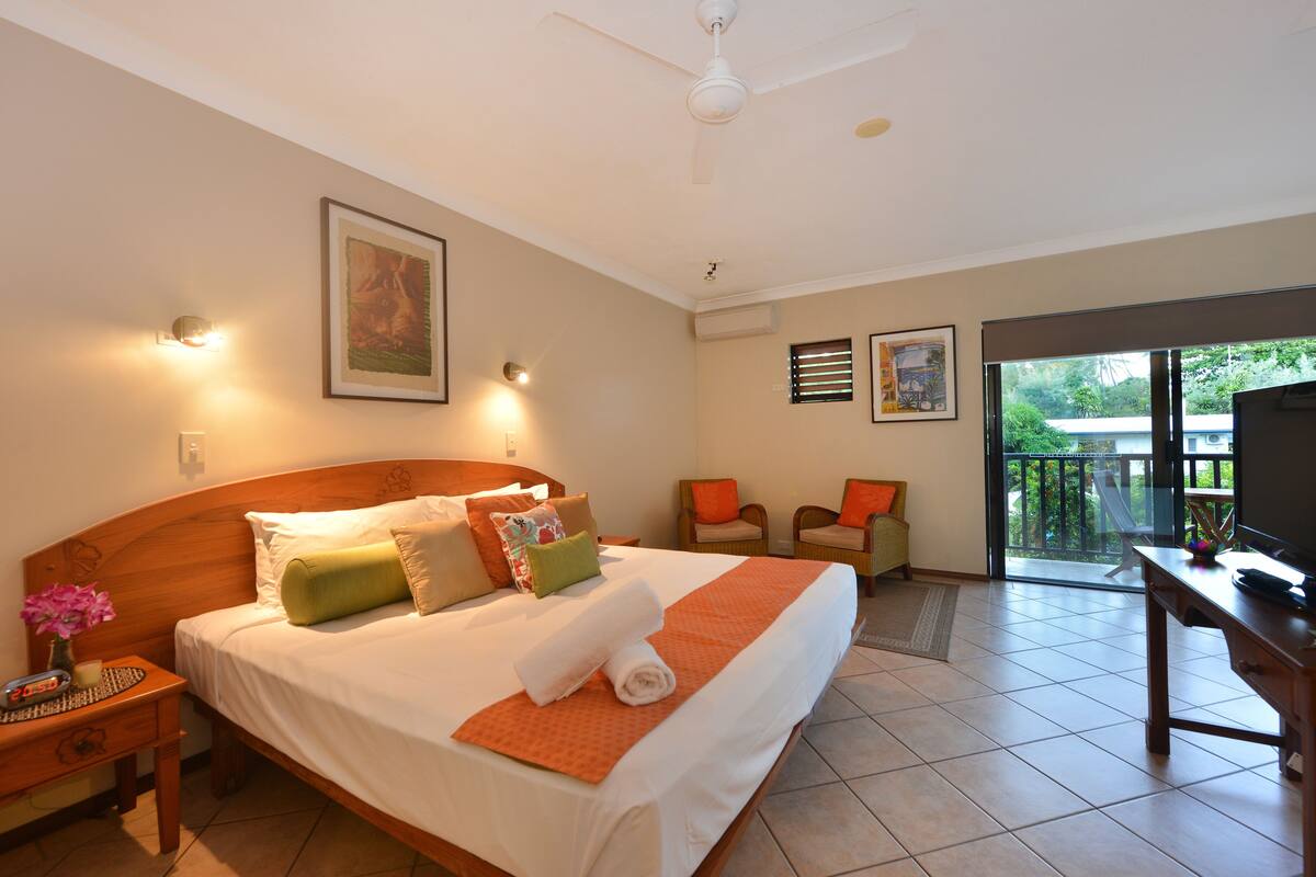 A hotel room with a bed, a desk, a chair, a television, and a balcony with a view.