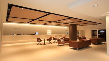 A modern hotel lobby with a reception desk, seating area, and a large pillar.