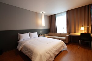 Hotellihuone, jossa on suuri sänky, työpöytä, tuoli, sohva ja ikkuna, jossa on verhot.