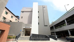 Une entrée d'hôtel moderne, avec une enseigne bien visible, un escalier menant à l'entrée et un parking en arrière-plan.