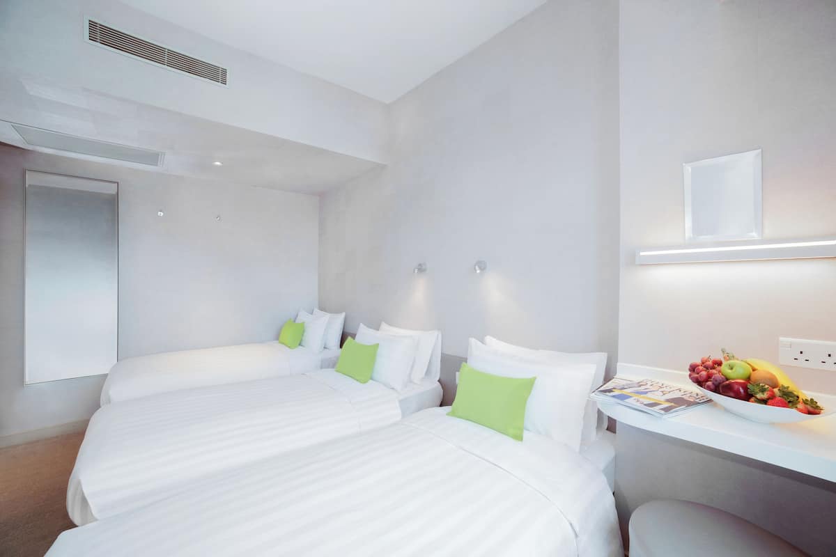 A hotel room with two beds, a desk with a fruit bowl, and a mirror on the wall.