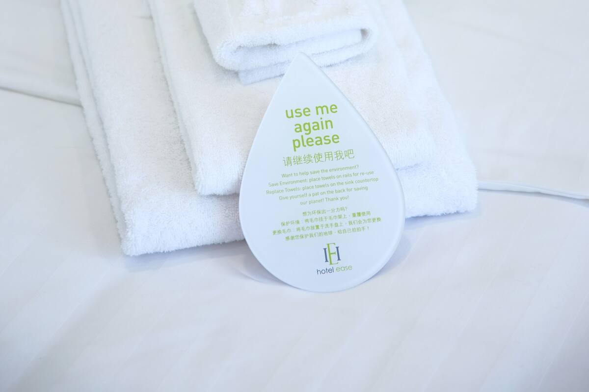 A neatly folded white towel with a tag on a bed with a green pillow.