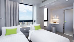 Een hotelkamer met twee bedden, een groot raam met uitzicht op de stad, een klein wastafeltje en een spiegel.