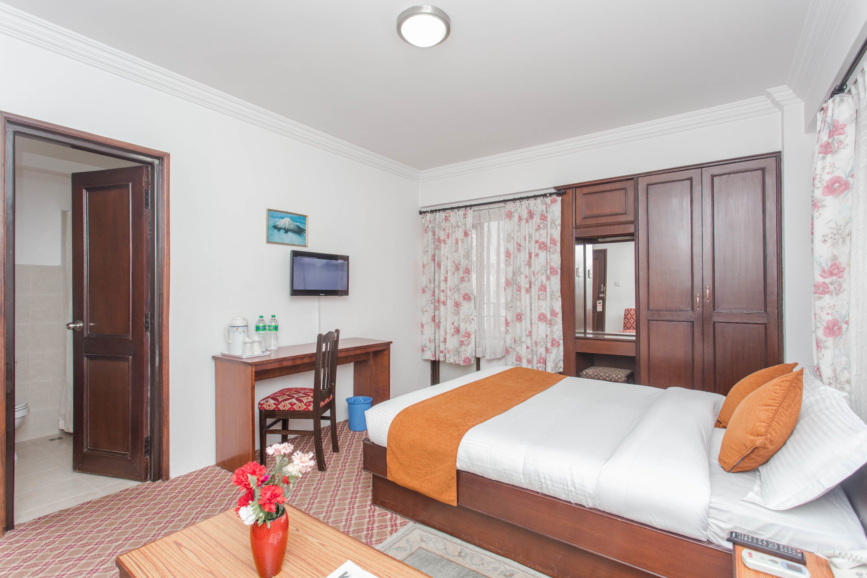 Een hotelkamer met een bed, een bureau met stoel, een televisie en een badkamers deur.