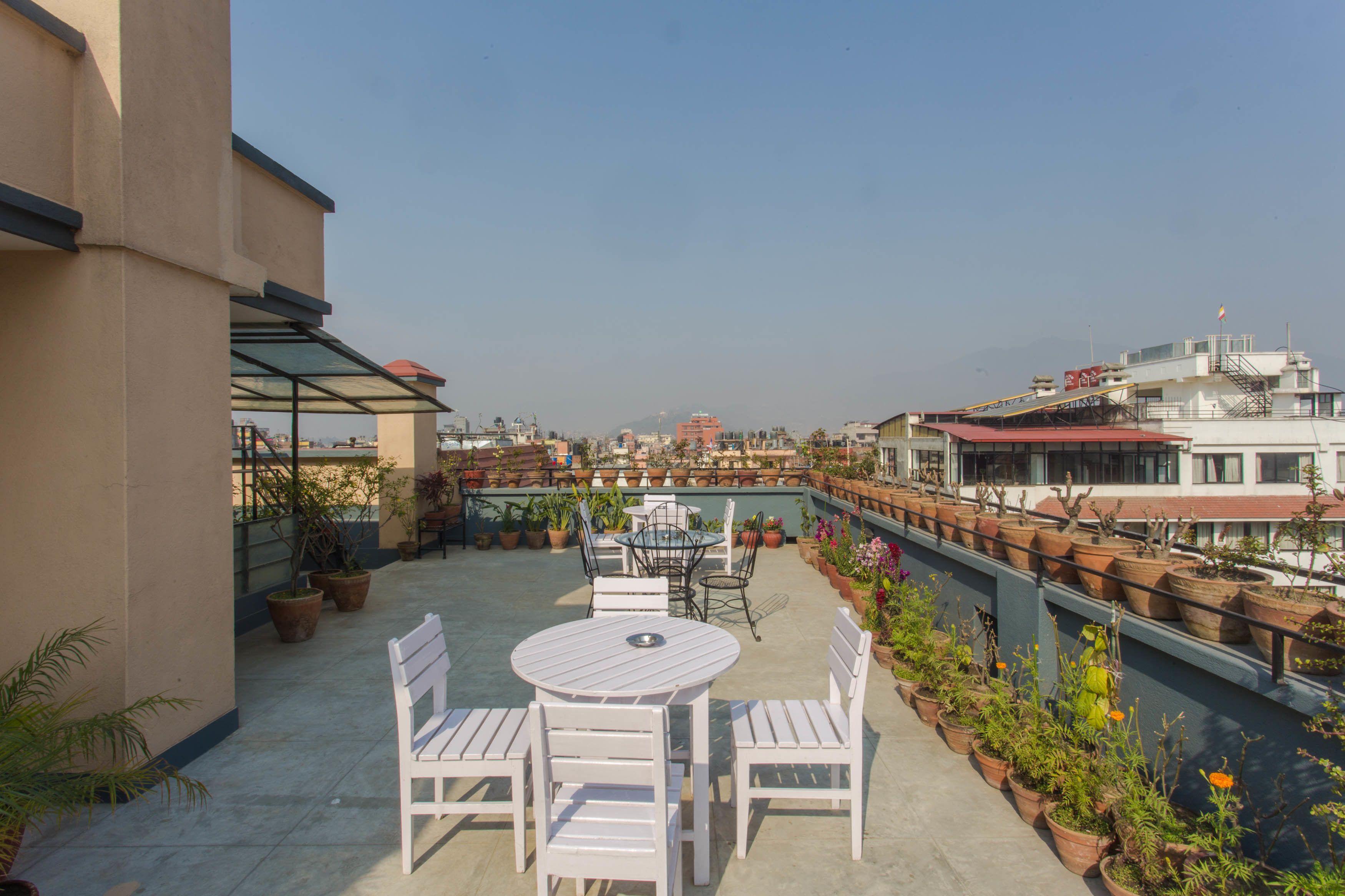 A rooftop terrace with a round table and chairs, potted plants, and a view of the cityscape.