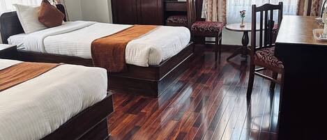 A hotel room with two beds, a wooden floor, a desk, and a chair.
