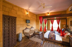 A traditional room with a wooden bed, two upholstered chairs, a small table, and a television.