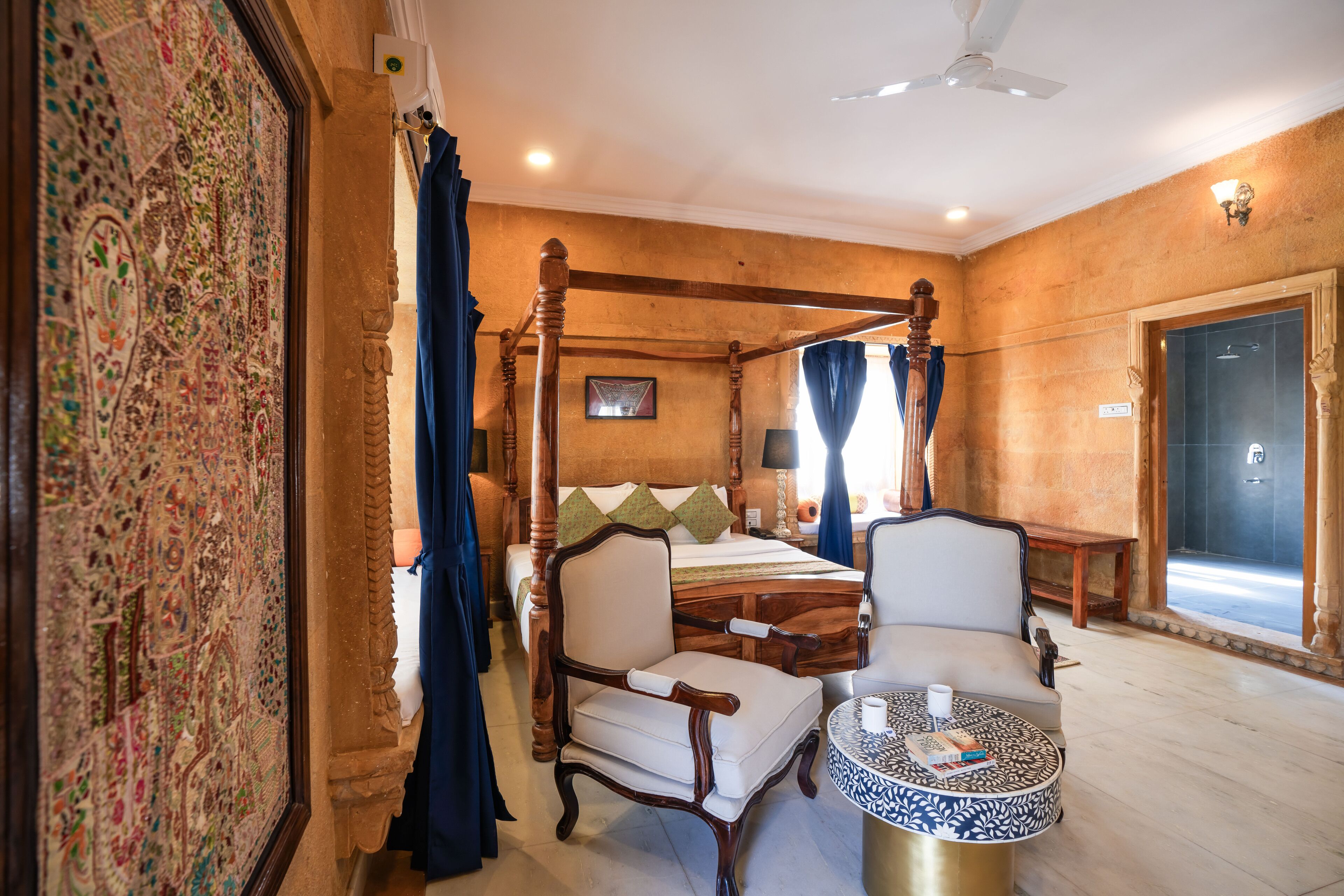 Una cama con dosel, un sillón, una mesa redonda de centro y un ventanal con cortinas.