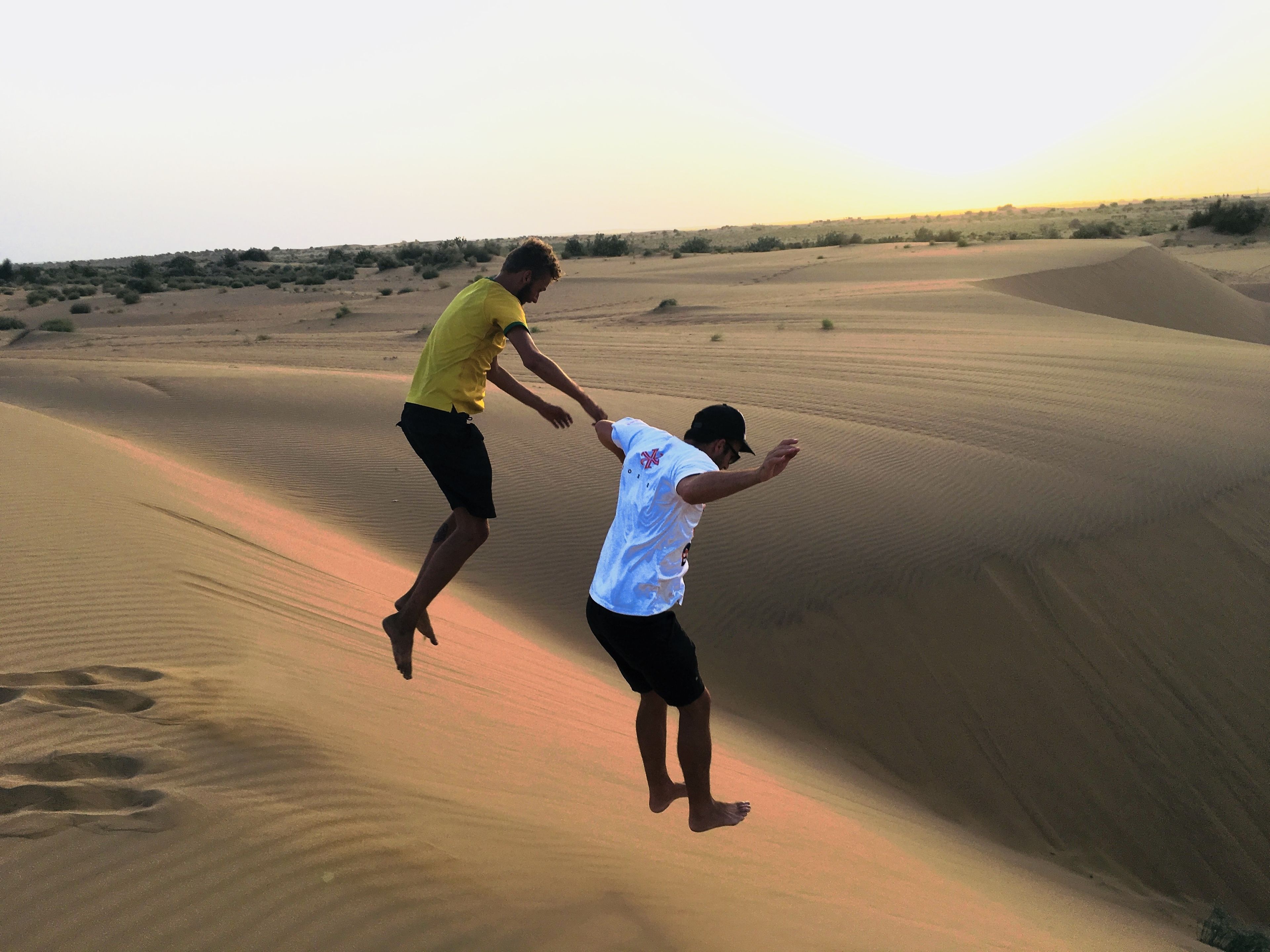 Duas pessoas saltando nas dunas de areia.