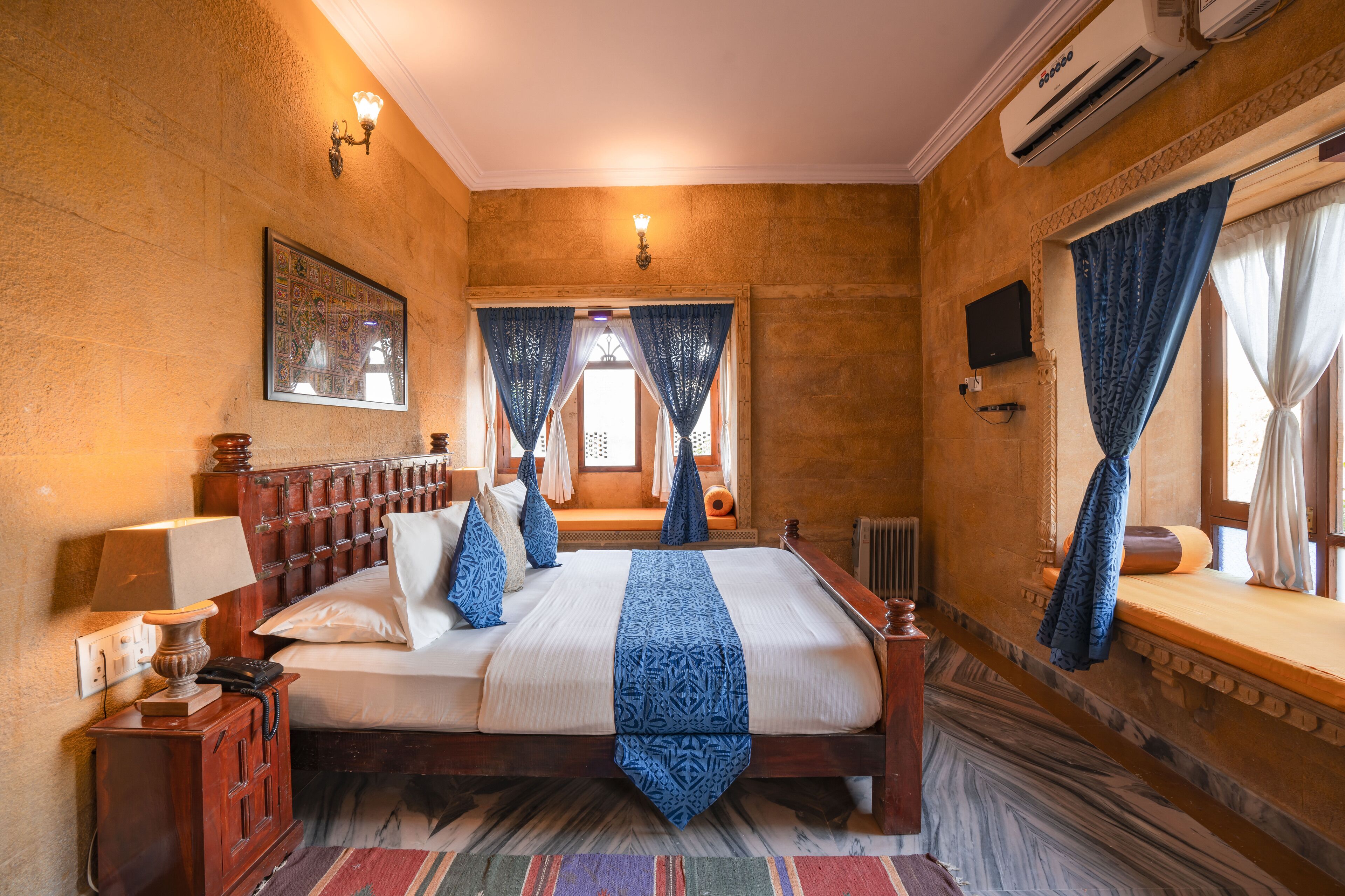 A bedroom with a large bed, a nightstand, a lamp, a wall-mounted TV, and a window with curtains.