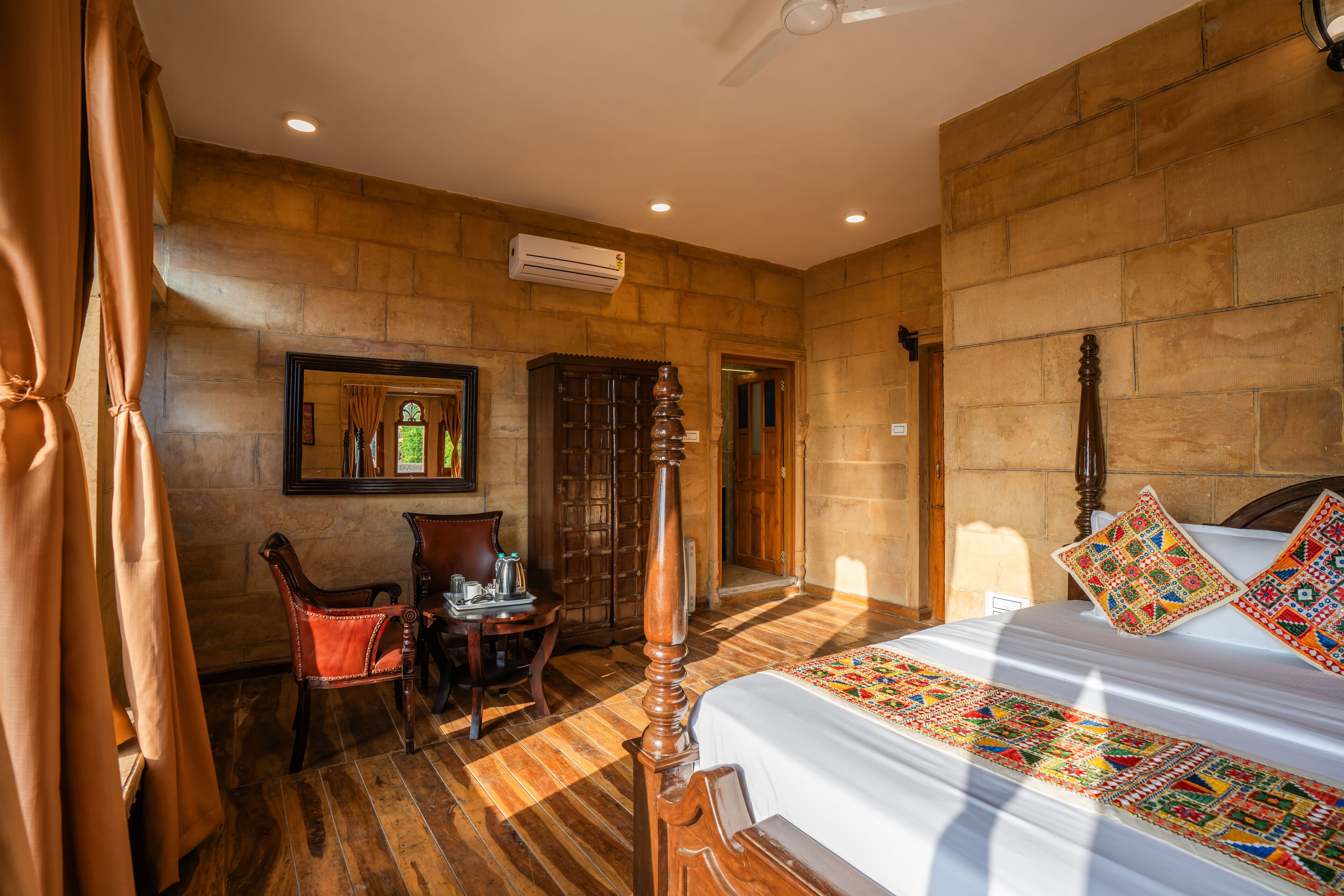 A hotel room with a large bed, a wooden headboard, a small table with a chair, and a mirror on the wall.