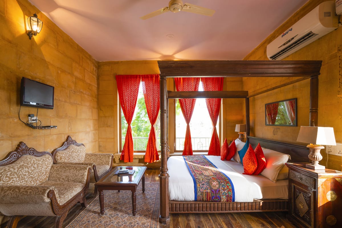 A traditional room with a four-poster bed, a sofa, a television, and a ceiling fan.