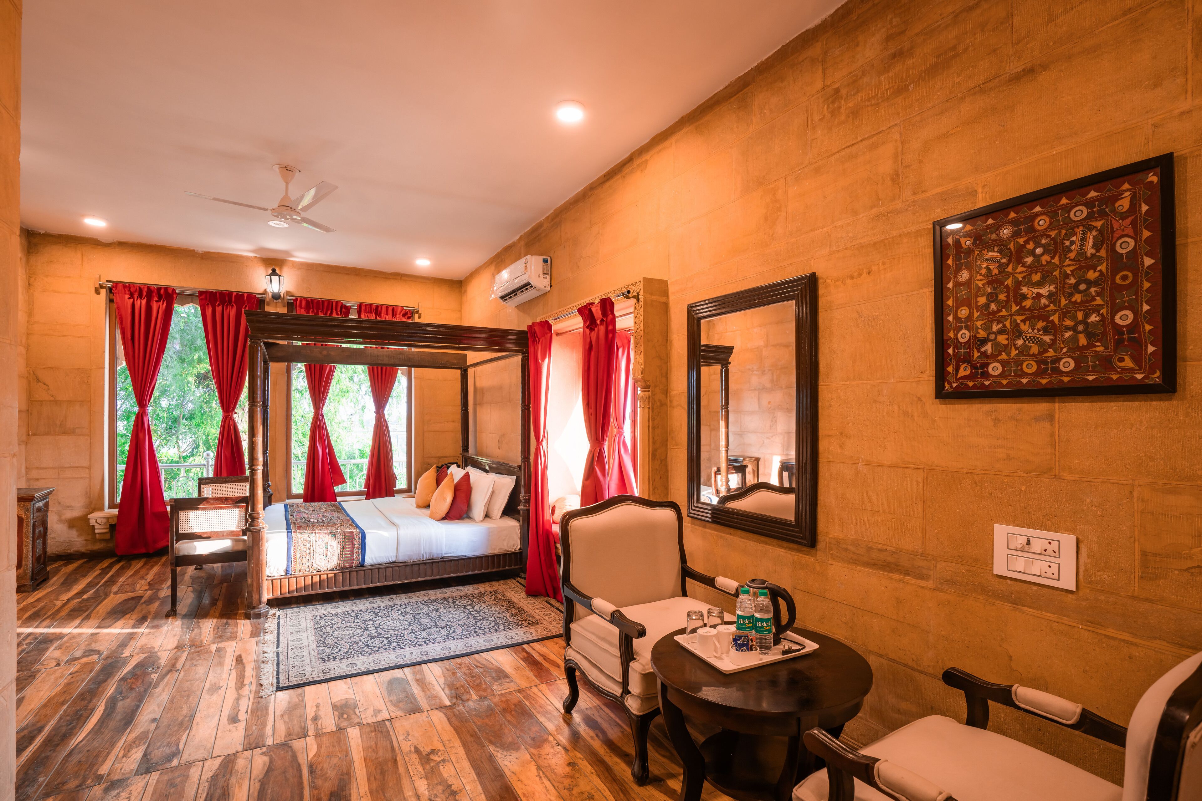 A room with a four-poster bed, a sitting area with a table and chairs, and a large mirror on the wall.