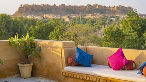Una terraza en la azotea con zona de estar, una planta en maceta y vista a una fortaleza histórica al fondo.