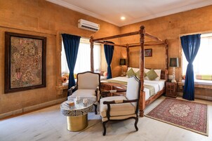 Una cama con dosel, una mesita de noche, una mesa redonda de centro y una alfombra grande en una habitación cálidamente iluminada con paredes de piedra.