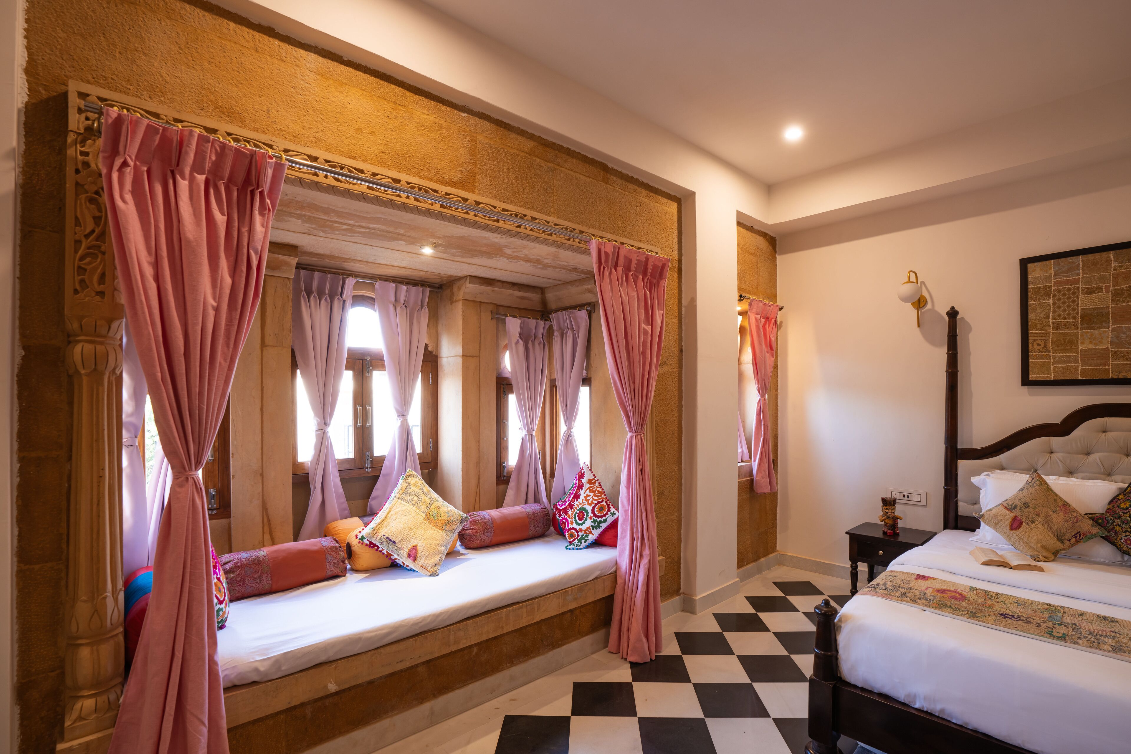 A bedroom with a large bed, a bench with pillows, a nightstand, and a wall-mounted lamp.