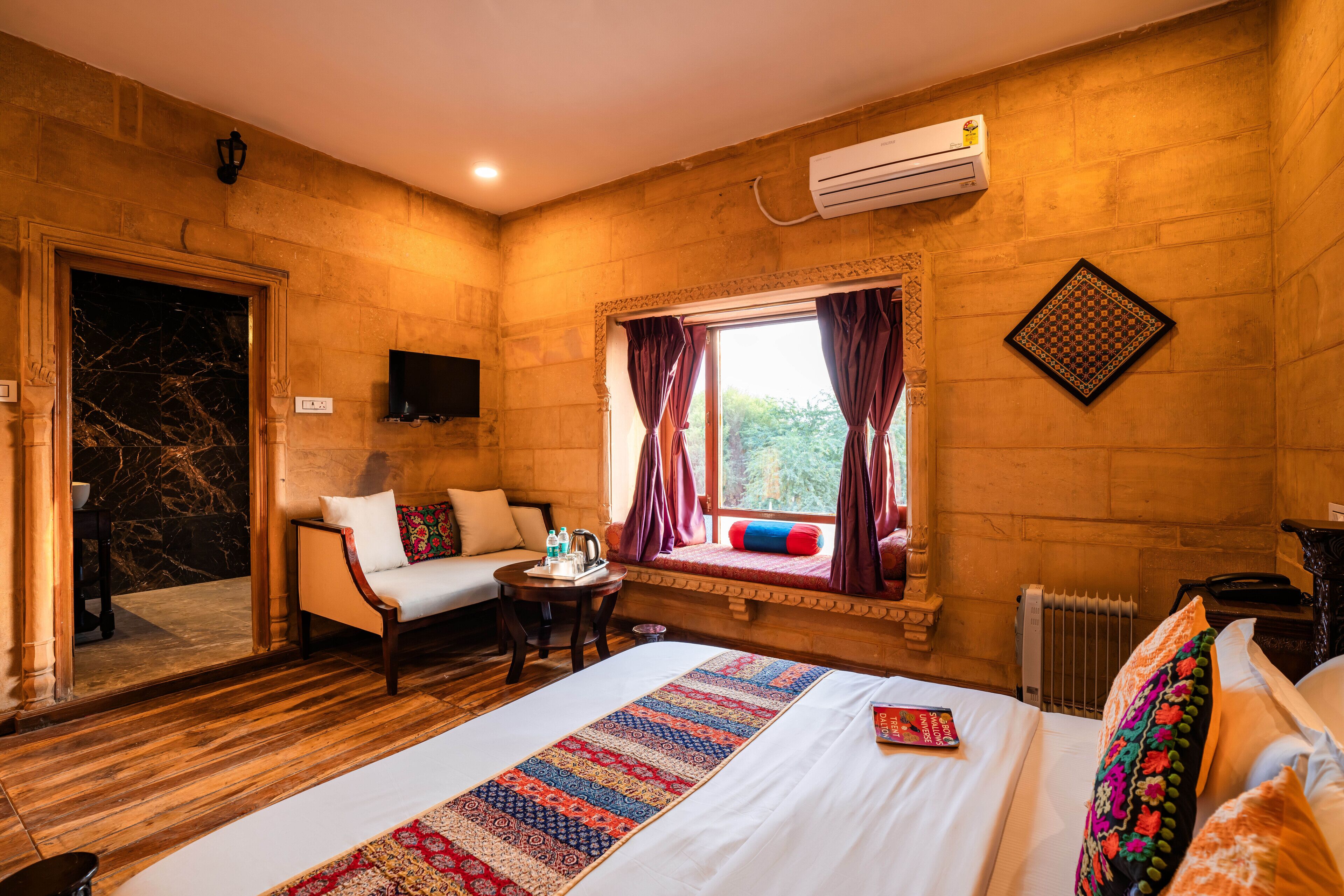 Una habitación de hotel con una cama grande, un sofá, una mesita y una ventana con cortinas.