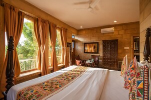 Un dormitorio amplio con una cama grande, un ventilador de techo y vistas al exterior a través de amplias ventanas.