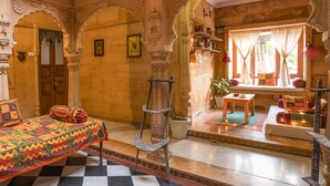 Una habitación tradicional con cama, una mesita y un ventanal con cortinas.