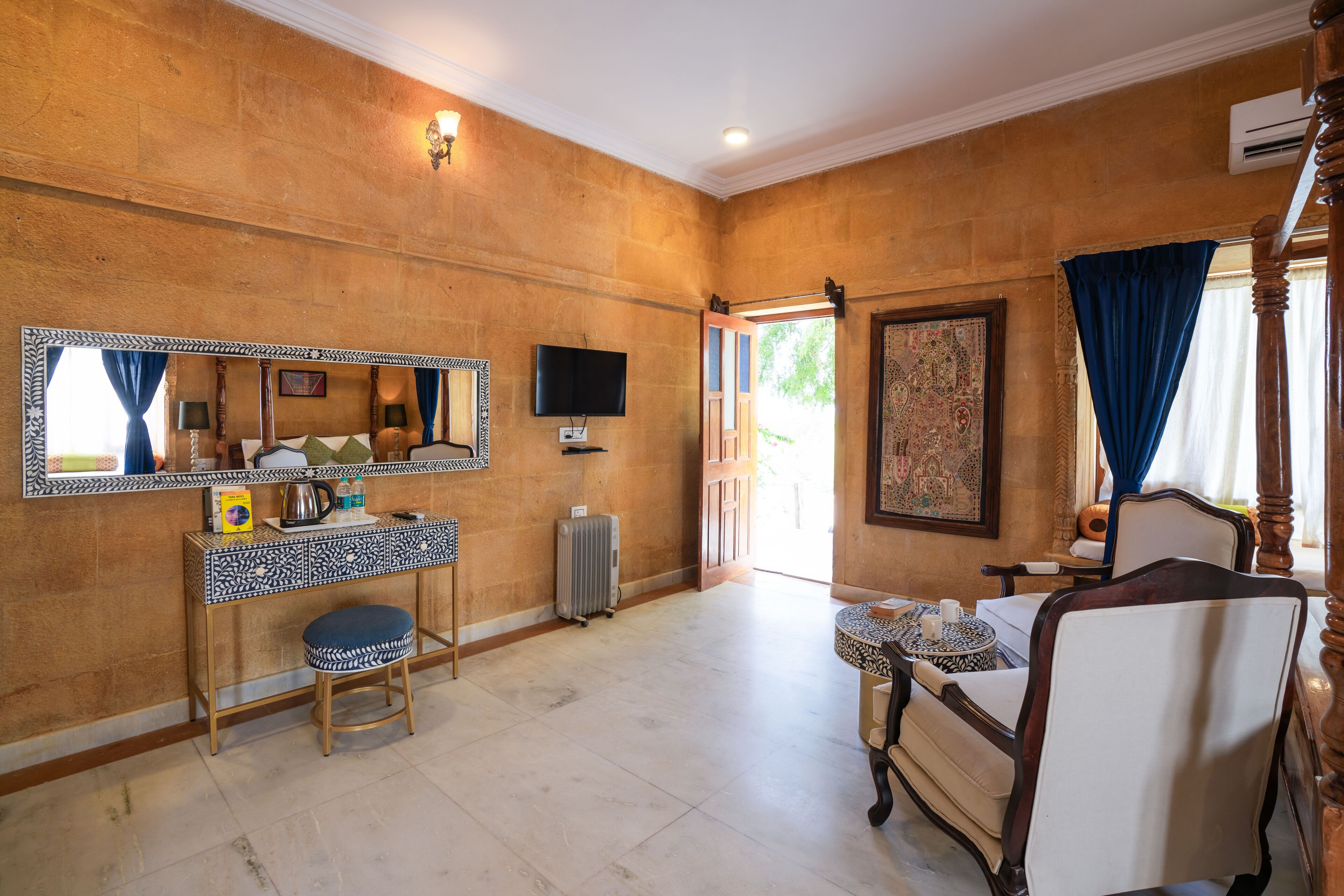 Una habitación con un espejo grande, televisión, radiador, una silla, una mesita y una ventana con cortinas.