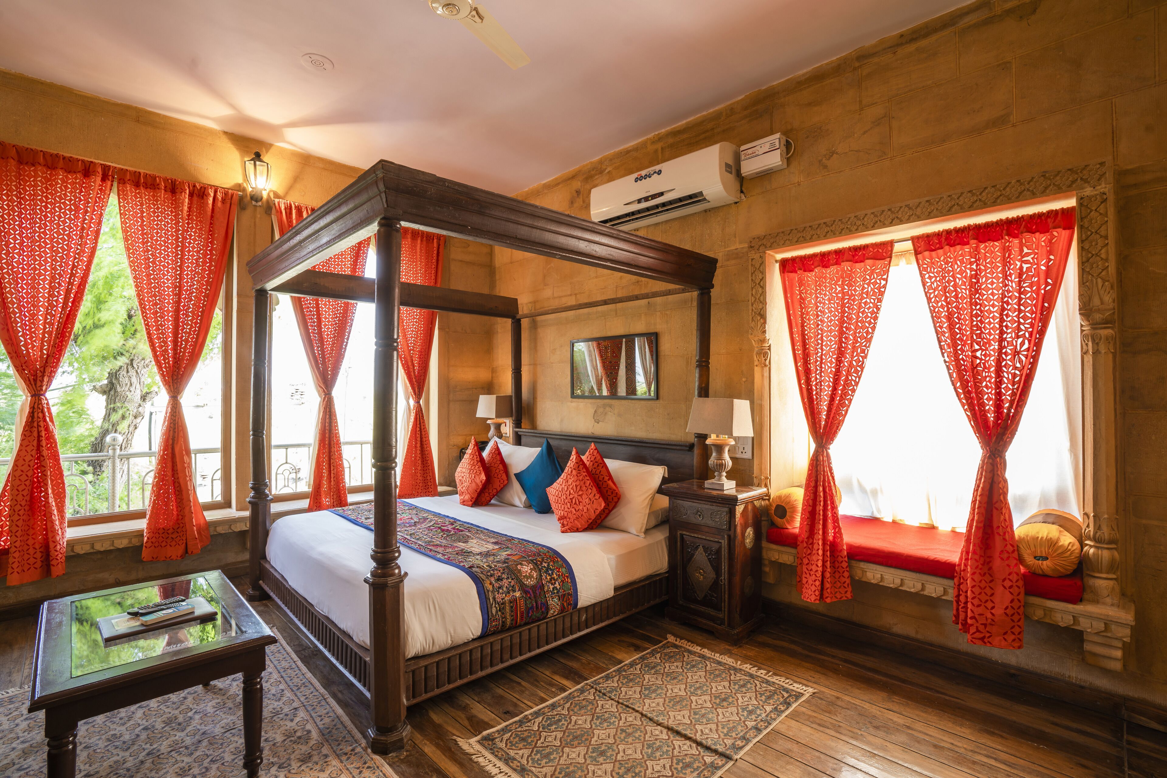 A four-poster bed with red curtains, a nightstand with a lamp, and a wooden floor.