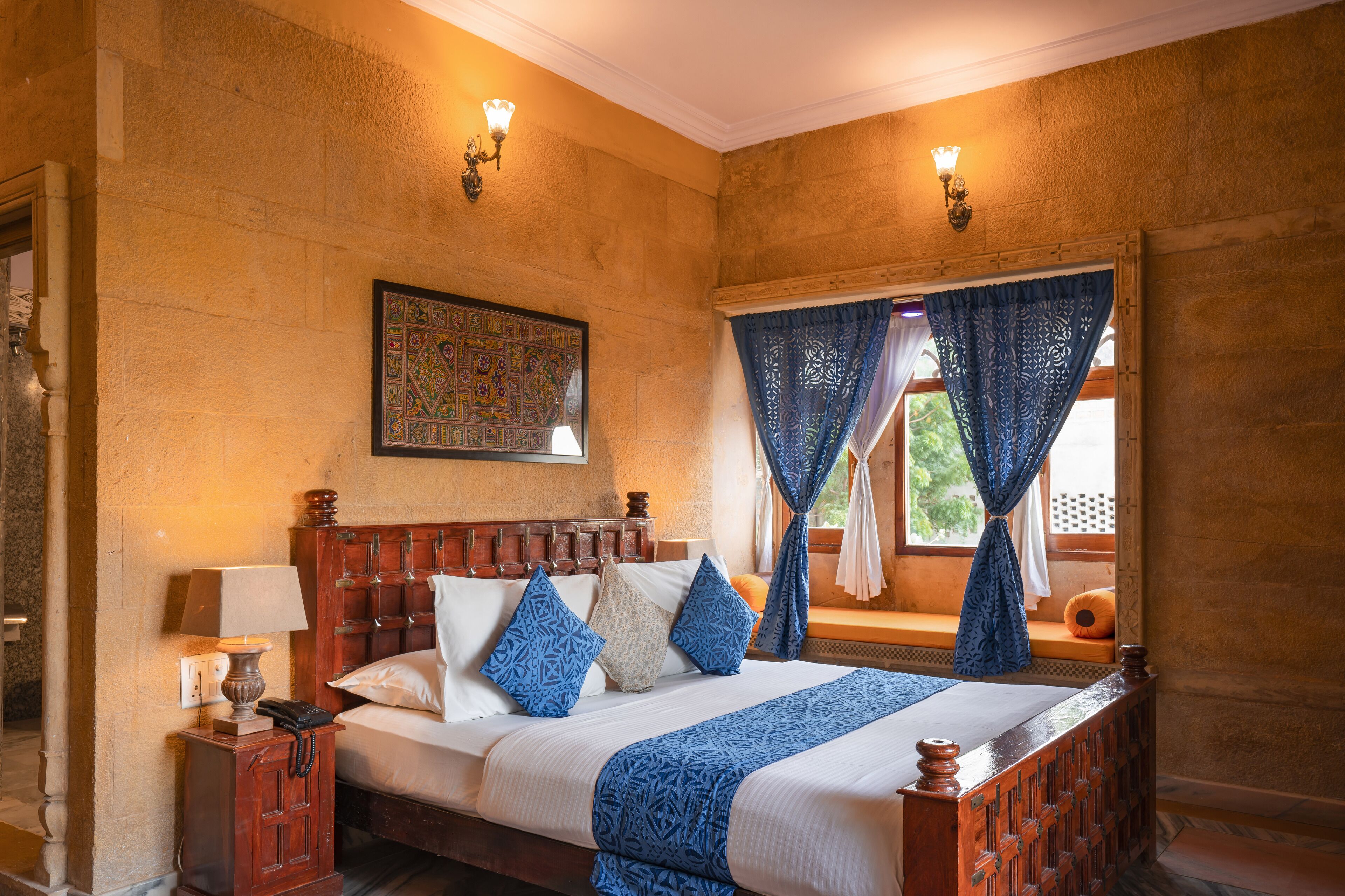 A room with a wooden bed, patterned pillows, a wall-mounted lamp, and a decorative tapestry.