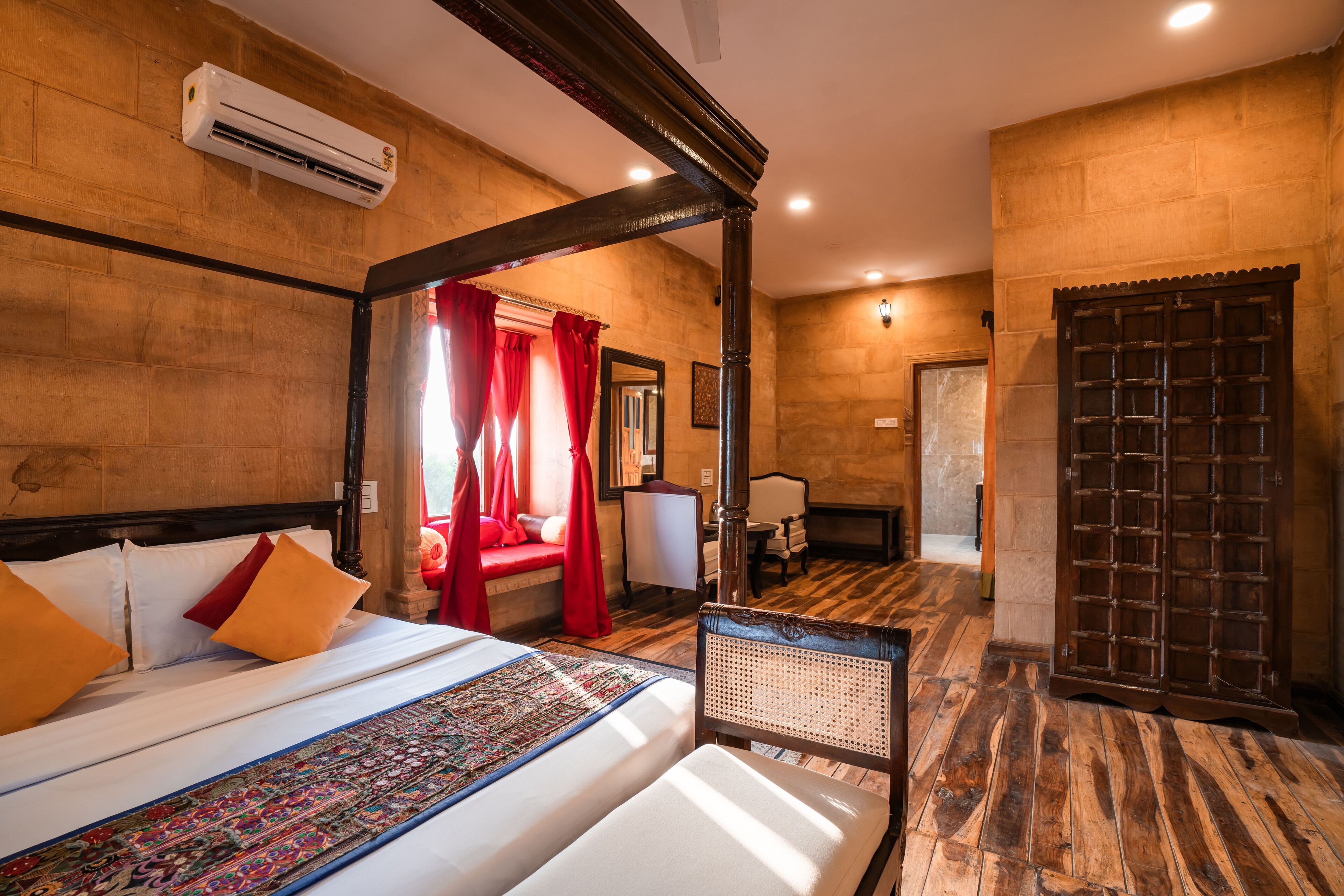 A hotel room with a large bed, a sitting area with a chair, a wooden floor, and a large wooden door.