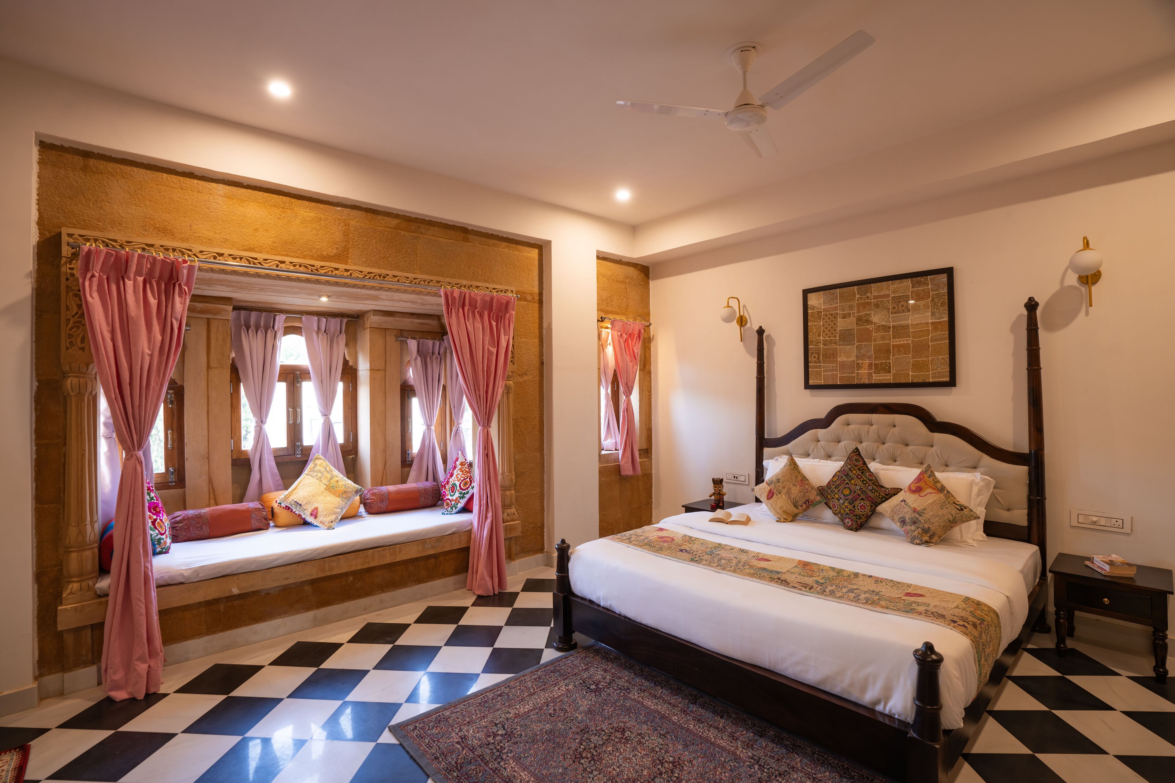 A bedroom with a checkered floor, a large bed with multiple pillows, a bedside table, and a ceiling fan.